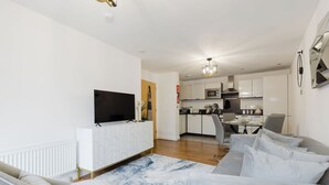 Een moderne woonkamer met een flatscreen televisie, een bank en een eethoek met een tafel en stoelen.