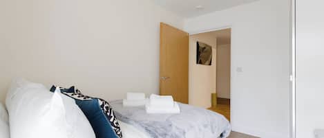A bedroom with a bed, pillows, and a door leading to another room.