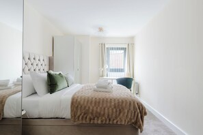 A hotel room with a bed, a chair, a window with curtains, and a ceiling light fixture. - Beautifully Presented 2BDR Flat in Canada Water (Greater London)