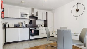 Een moderne keuken met witte kasten, een magnetron, een fornuis en een eethoek met een grijze stoel en tafel.