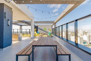 Terraço no telhado com mesa de madeira, cadeiras e luzes de corda.