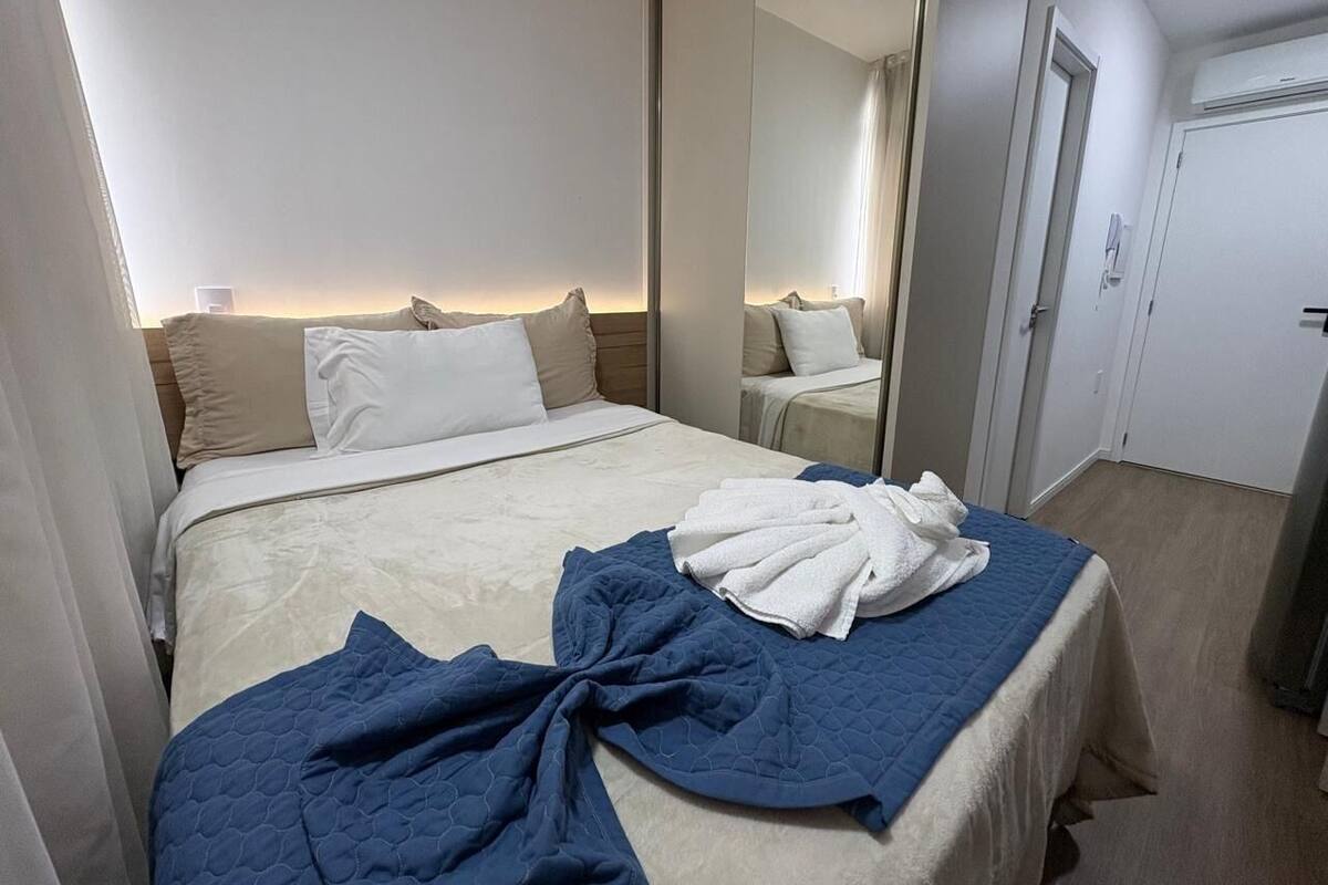 Quarto de hotel com cama, espelho, porta e janela.