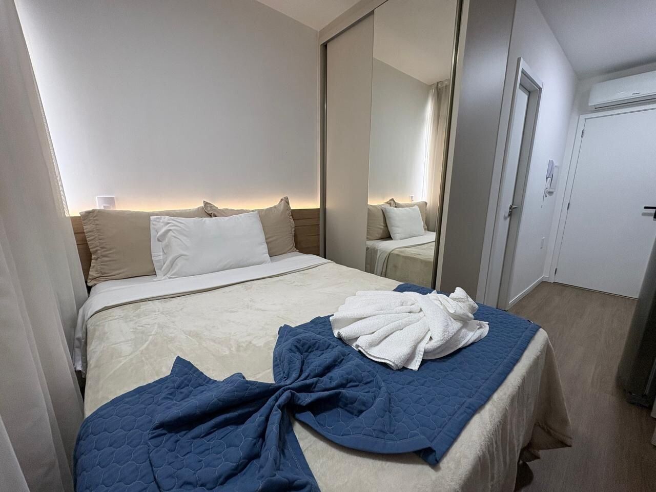Quarto de hotel com cama, espelho, porta e janela.