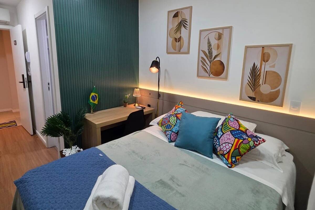 Quarto de hotel com cama, mesa de cabeceira, luminária e arte na parede.