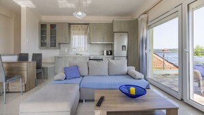 A modern living room with a sofa, a coffee table, and a view of the kitchen and balcony. - Sunrise Villa No 1 - Agios Nikolaos Halkidiki (Vourvourou)