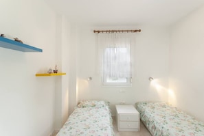 A small, simple room with two single beds, a small table, and a window with a curtain. - Nature Green House by RentalsPro - Akti Elia Halkidiki (Nikiti)
