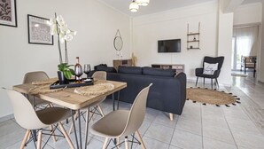 A modern living room with a dining area, a sofa, a TV, and a chandelier.