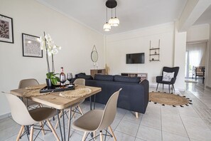 Ein modernes Wohnzimmer mit Essbereich, einer Couch, einem Fernseher und einer Chandelüster.