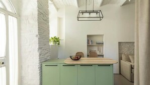 Uma cozinha com bancada verde, luminária pendente e estante ao fundo.