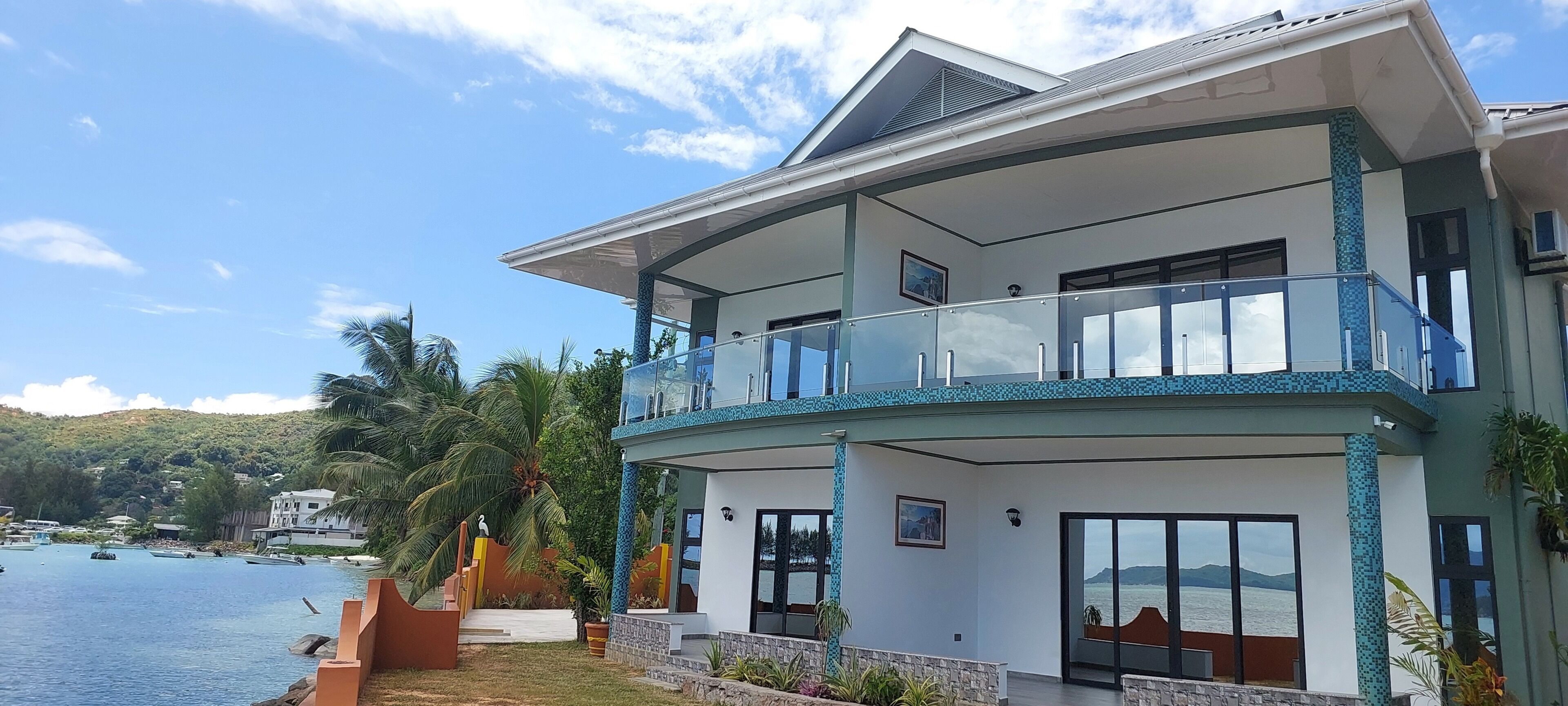 A modern two-story house with a balcony, large windows, and a view of the water.
