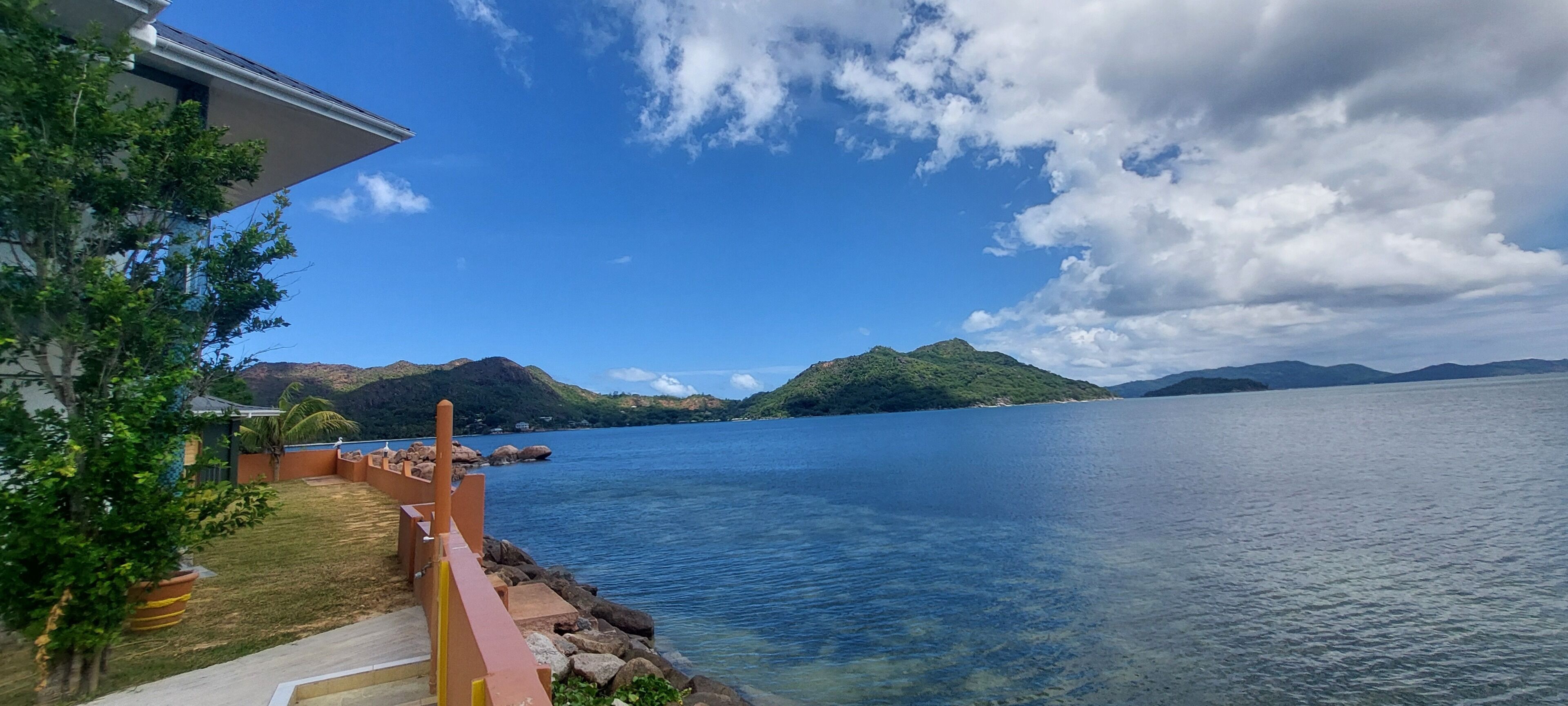 Une vue sur la côte, avec une eau limpide, une terrasse en bois et des montagnes à l’horizon.