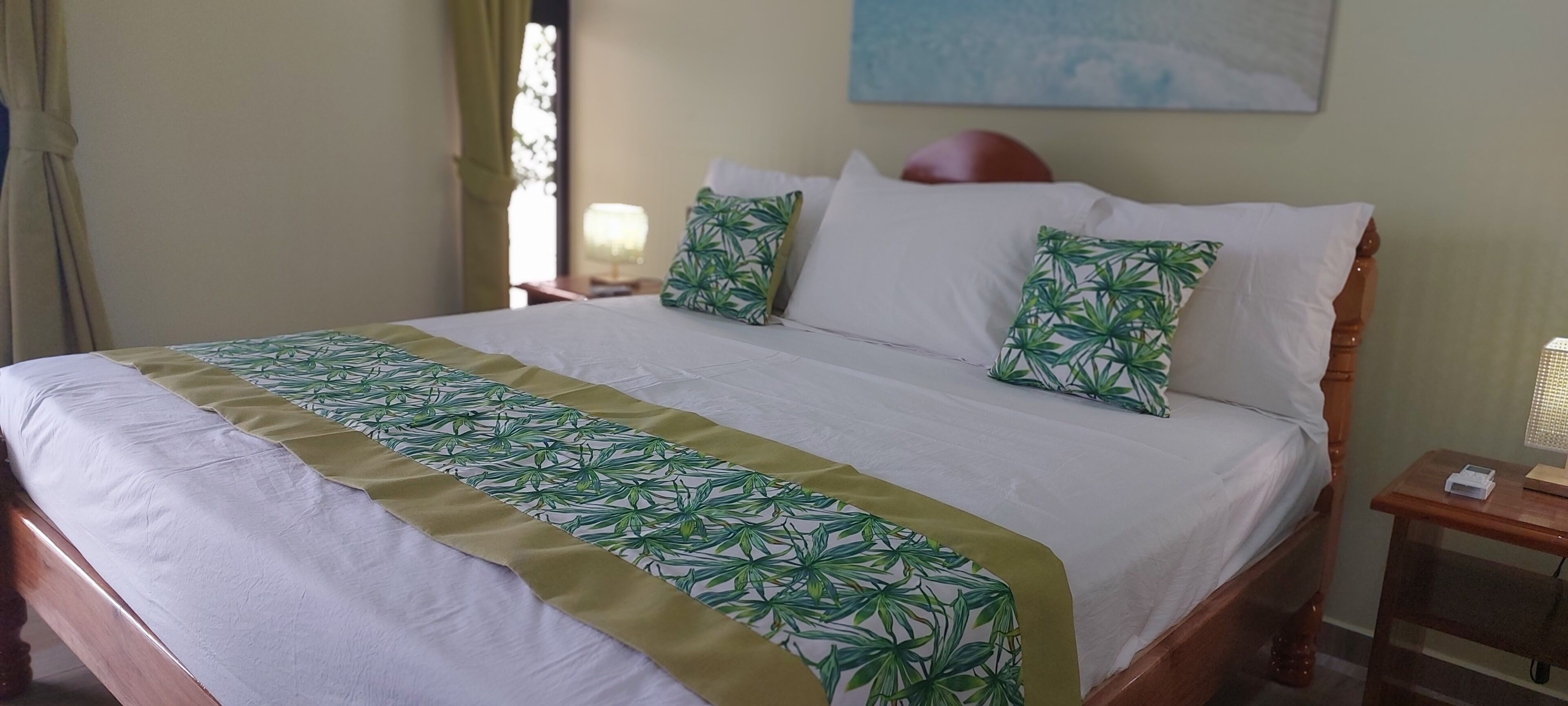 Een bed met een bedspreidek met een groen bladpatroon, witte kussens en een houten hoofdbord.