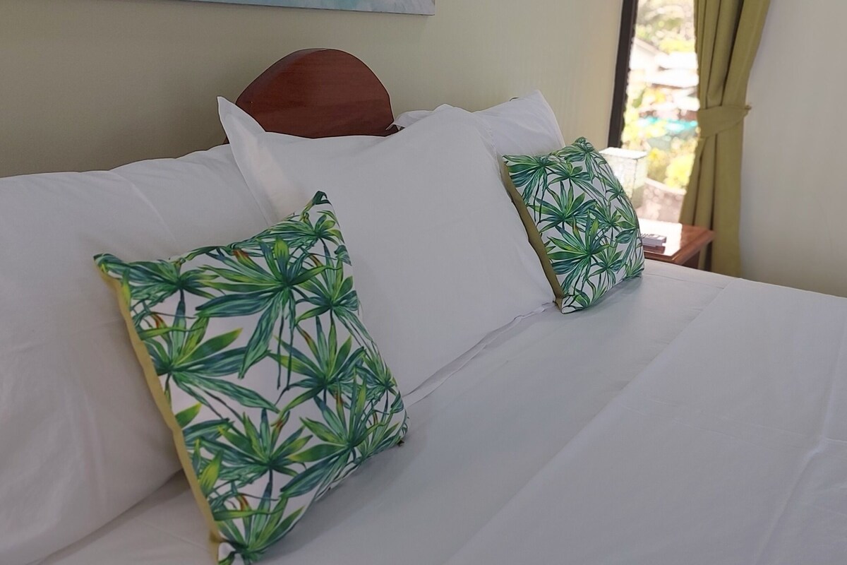 A bed with white bedding and two green leaf-patterned pillows.