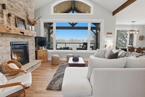 A modern living room with a fireplace, a large window, and a cozy seating area. - Stonehedge Lakehouse - Hot Tub - Pool Table (Kawartha Lakes)
