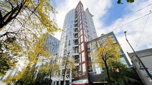 A modern high-rise building with a prominent red and white facade, surrounded by trees with yellow leaves. - Urban Loft Perch • City Views • Free Parking (Vancouver)