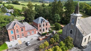 A large brick building with a prominent tower, surrounded by greenery and a paved area with a parked car. - La Cure de Rièzes, Chimay, newly renovated cottage for 12 with sauna (Chimay)