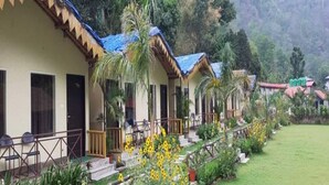 A row of bungalow-style accommodations with thatched roofs, surrounded by lush greenery and a well-maintained lawn. - Nakshatra Resort (Rishikesh)