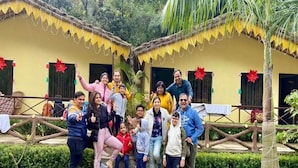 A group of people posing in front of a building with a thatched roof and a fence. - Nakshatra Resort (Rishikesh)