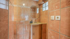 Un baño con pared de azulejos, un lavamanos, un espejo y una ducha.