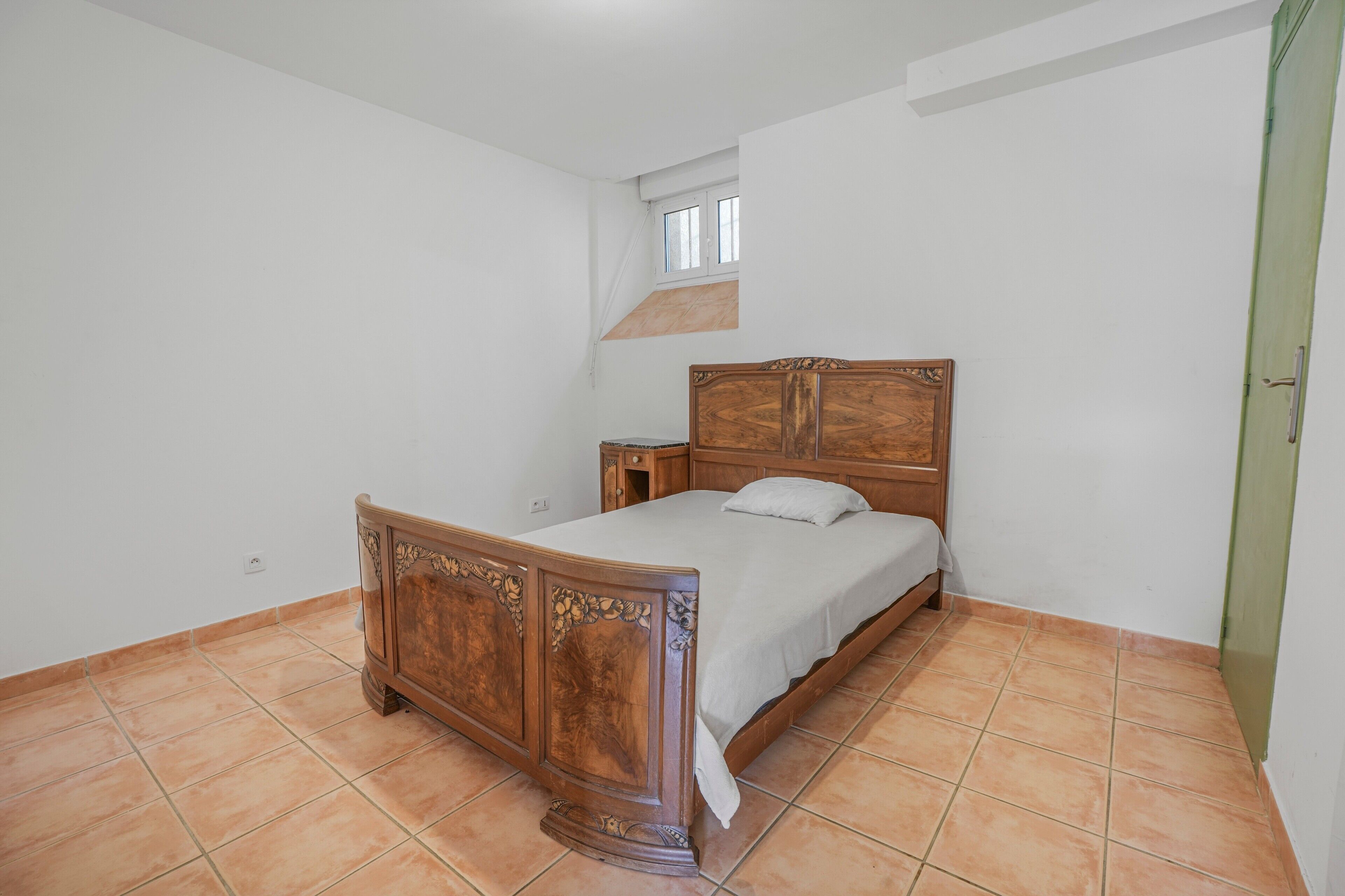 A bedroom with a wooden bed, a nightstand, a window, and a green door.