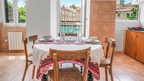 Comedor con una mesa dispuesta para cuatro personas, vista de edificios a través de una ventana y suelo de baldosas.