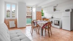 Una cocina moderna con armarios blancos, un área de comedor con mesa y sillas, una lavadora y un sofá gris.