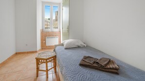 Una habitación pequeña con una cama, una silla, una ventana y una puerta.