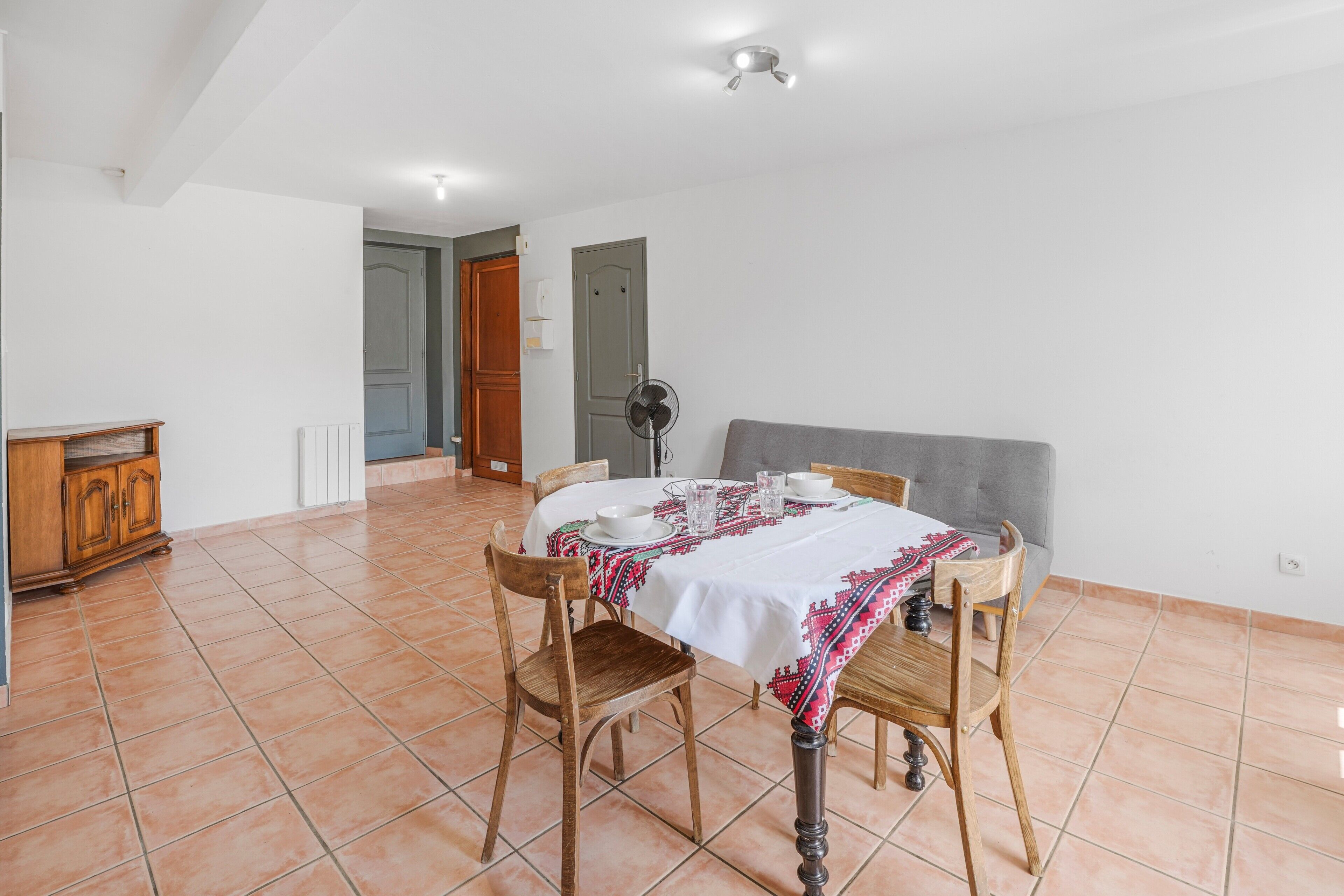 A dining area with a table set for four, a grey sofa, and a wooden cabinet.