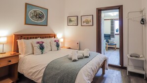 A neatly arranged bedroom with a bed, bedside lamps, a wooden headboard, and a door leading to another room. - Islay Cottage (Kingussie)