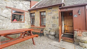 A stone building with a wooden door, a bench, and a sign that reads 'Islay Cottages.' - Islay Cottage (Kingussie)