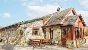 A stone building with a wooden door, windows, and a bench. - Islay Cottage (Kingussie)