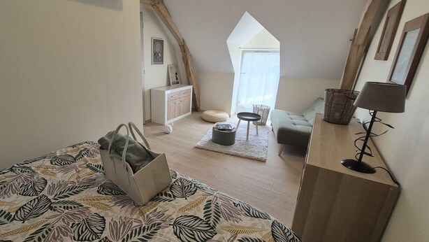 A loft bedroom with a sloped ceiling, a bed with a leaf-patterned bedspread, a bedside table with a lamp, a dresser, and a view of the outside. - Large gite for up to 8 people, close to Beauval and the Loire castles (Mareuil-sur-Cher)