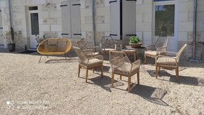 A stone building with a gravel patio, outdoor seating with wicker chairs, and a small table with a plant. - Large gite for up to 8 people, close to Beauval and the Loire castles (Mareuil-sur-Cher)