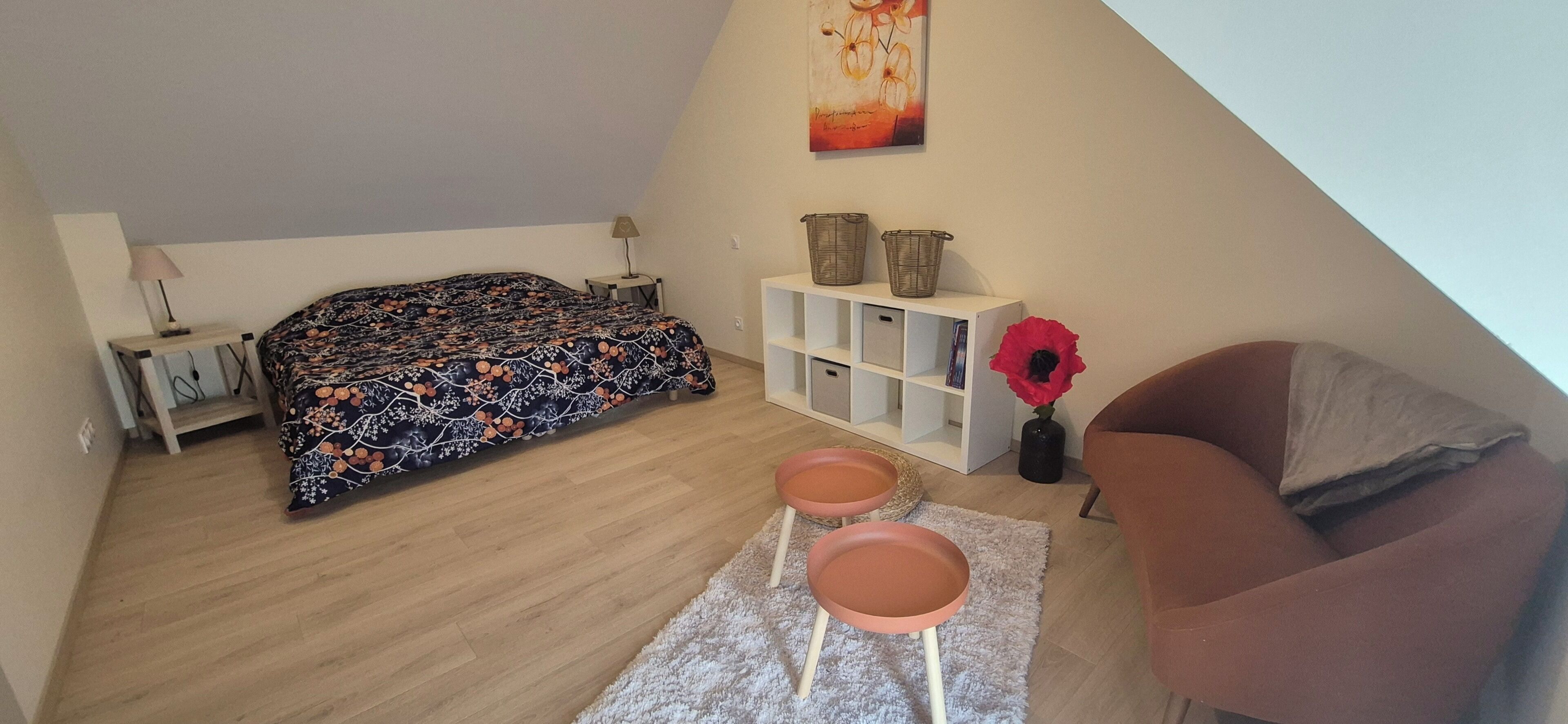 Een slaapkamer met een bed, een nachtkastje, een lamp, een boekenplank, een stoel en een klein tafeltje met twee krukken.