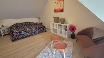 Een slaapkamer met een bed, een nachtkastje, een lamp, een boekenplank, een stoel en een klein tafeltje met twee krukken.