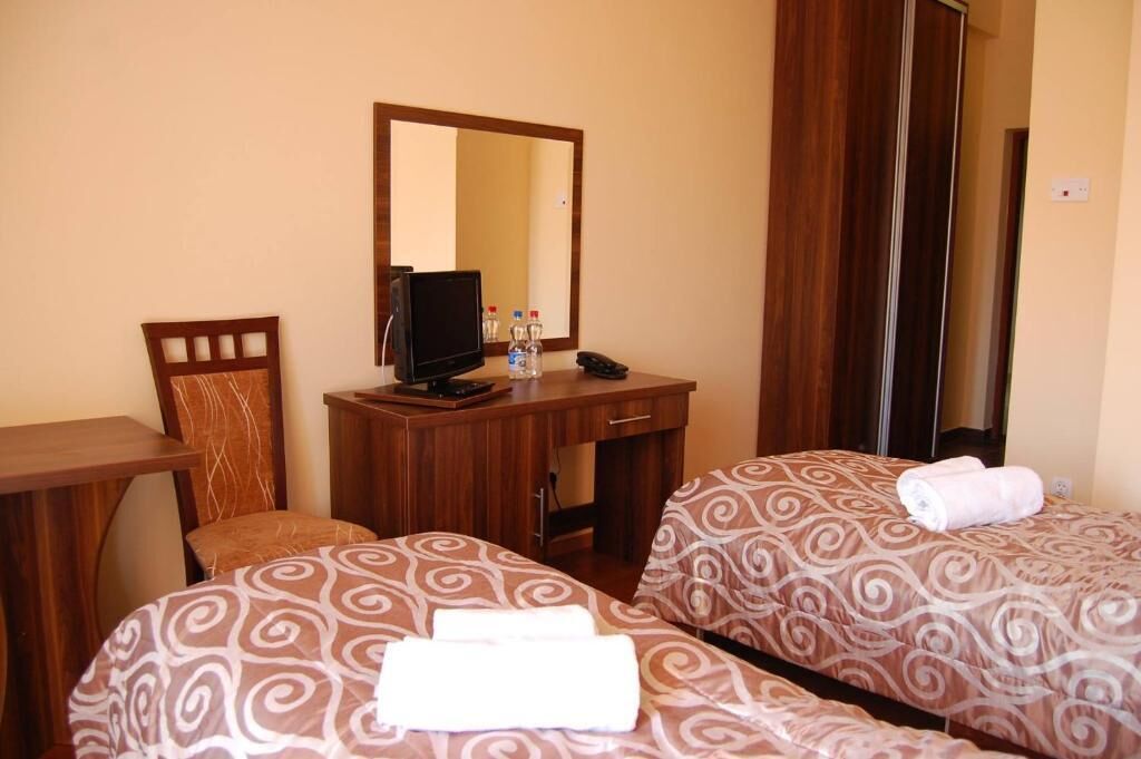 Habitación de hotel con dos camas, un escritorio, una silla, un televisor y un espejo.