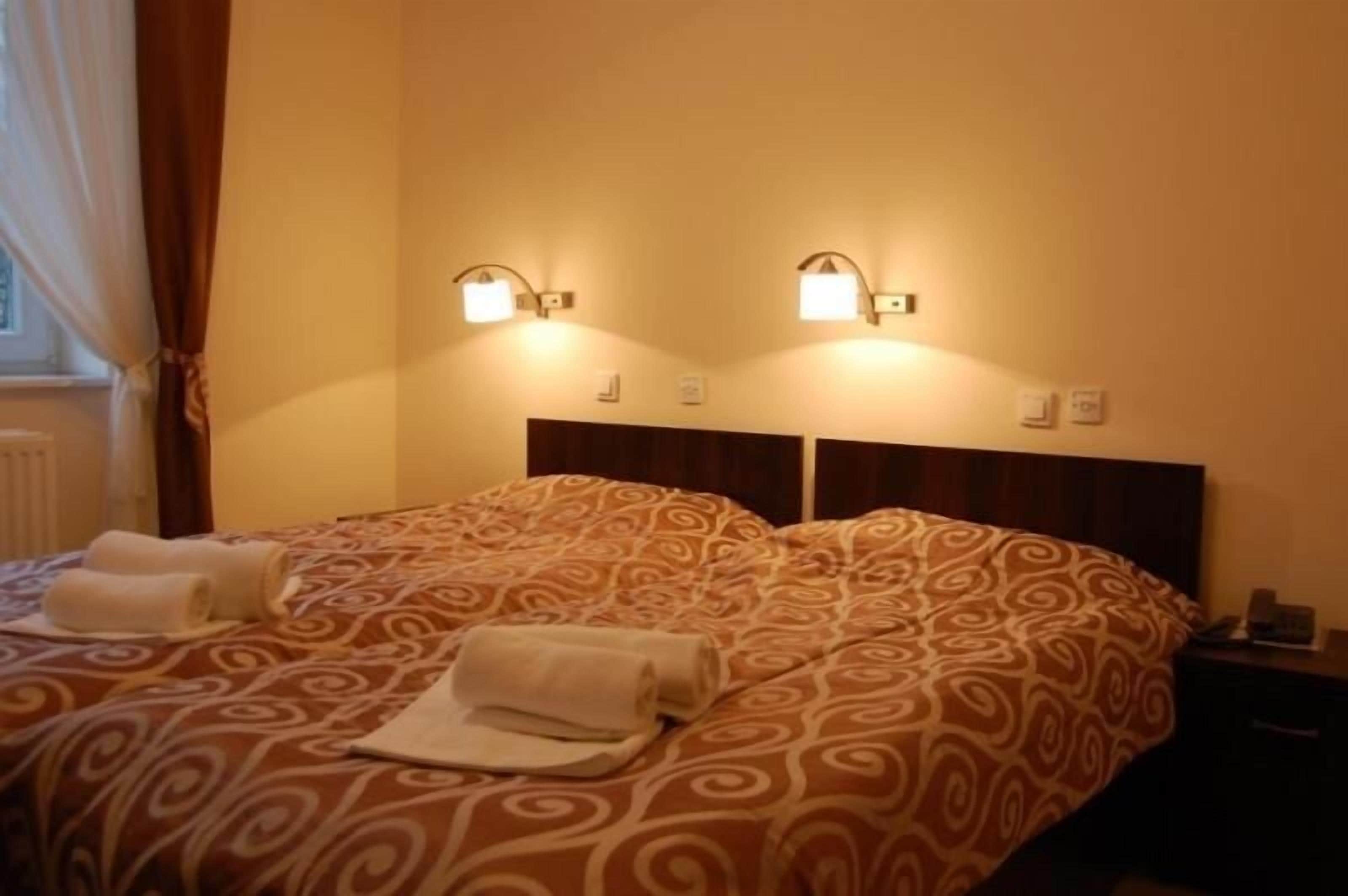 Ein Hotelzimmer mit zwei Betten, jedes mit einer gemusterten Tagesdecke, zwei Wandleuchten und einem Nachttisch mit Telefon.