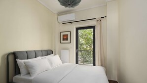 Une chambre à coucher comprenant un lit, un appareil de climatisation, une fenêtre donnant sur un espace verdoyant et un tableau encadré accroché au mur.