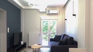 A modern living room with a sofa, a TV, a small table, and a window with a view of greenery. - Myrto by halu! - Cozy apt close to Ippokrateio hospital (Thessaloniki)