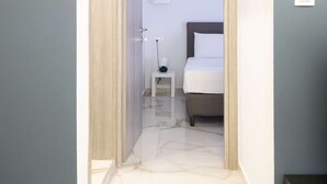 A narrow hallway leading to a bedroom with a bed, bedside table, and a wall-mounted light. - Myrto by halu! - Cozy apt close to Ippokrateio hospital (Thessaloniki)