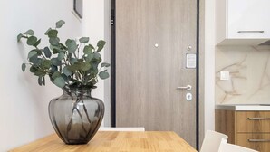 A dining area with a wooden table and white chairs, a potted plant, a door, and a kitchen area with marble countertops. - Myrto by halu! - Cozy apt close to Ippokrateio hospital (Thessaloniki)