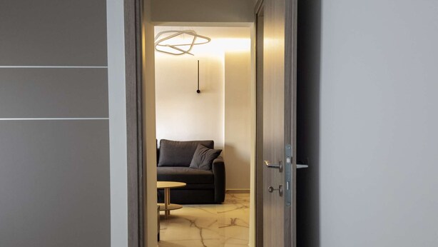A modern interior with a marble floor, a dark sofa with cushions, a small round table, and a hanging light fixture. - Myrto by halu! - Cozy apt close to Ippokrateio hospital (Thessaloniki)