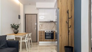 A modern kitchen with white cabinets, a wooden door, and a black trash bin. - Myrto by halu! - Cozy apt close to Ippokrateio hospital (Thessaloniki)