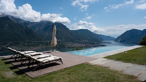 Un espace aménagé au bord de la piscine, avec des chaises longues et un parasol, offrant une vue sur un lac et des montagnes.