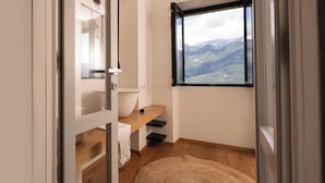 Une salle de bain avec une grande fenêtre, un lavabo blanc et une étagère en bois.