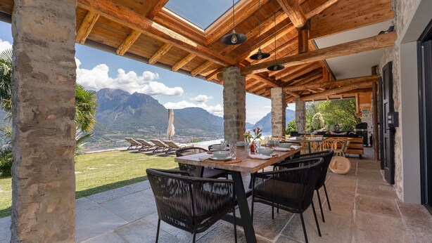 Un espace extérieur abrité, aménagé pour les repas, avec une table dressée pour quatre personnes, entourée de chaises, et offrant une vue sur un paysage montagneux.