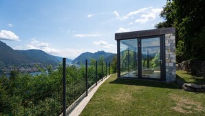 Une structure moderne en verre, agrémentée d’éléments en pierre, qui offre une vue imprenable sur un paysage montagneux et un plan d’eau.