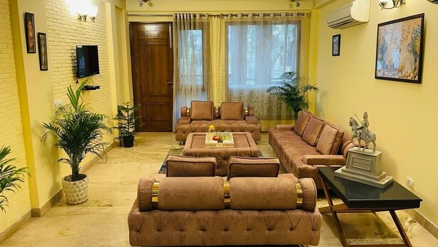 A living room with a sofa set, a coffee table, a TV, and a statue. - Fortune Home Service Apartment 4Bhk D-36 (New Delhi)