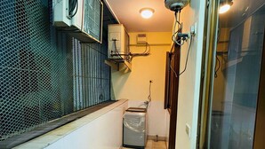 A narrow corridor with tiled walls, a trash bin, and a window with a metal grill. - Fortune Home Service Apartment 4Bhk D-36 (New Delhi)
