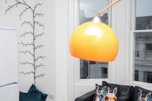 A room with a modern lamp, a branch light decoration, and a sofa with a colorful cushion.